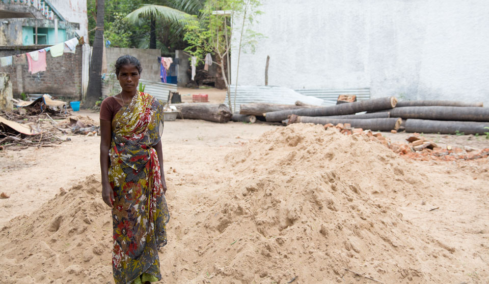Manjula stands beside a mound of sand where her new home will be built